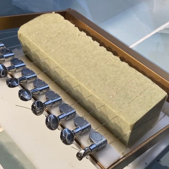 A rectangular block of pale yellow-green wax or beeswax displayed in a clear glass display case, with several silver metal tools or clips arranged along one side.